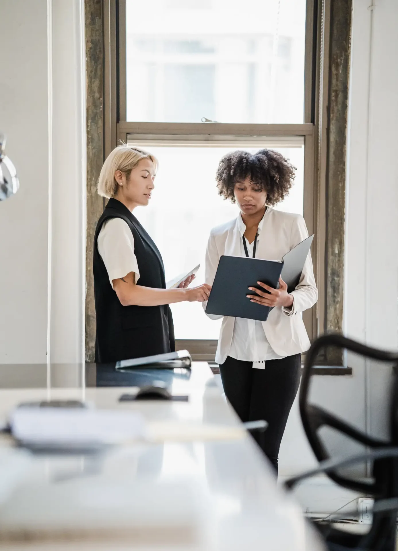 Two women are standing in a room with papers.